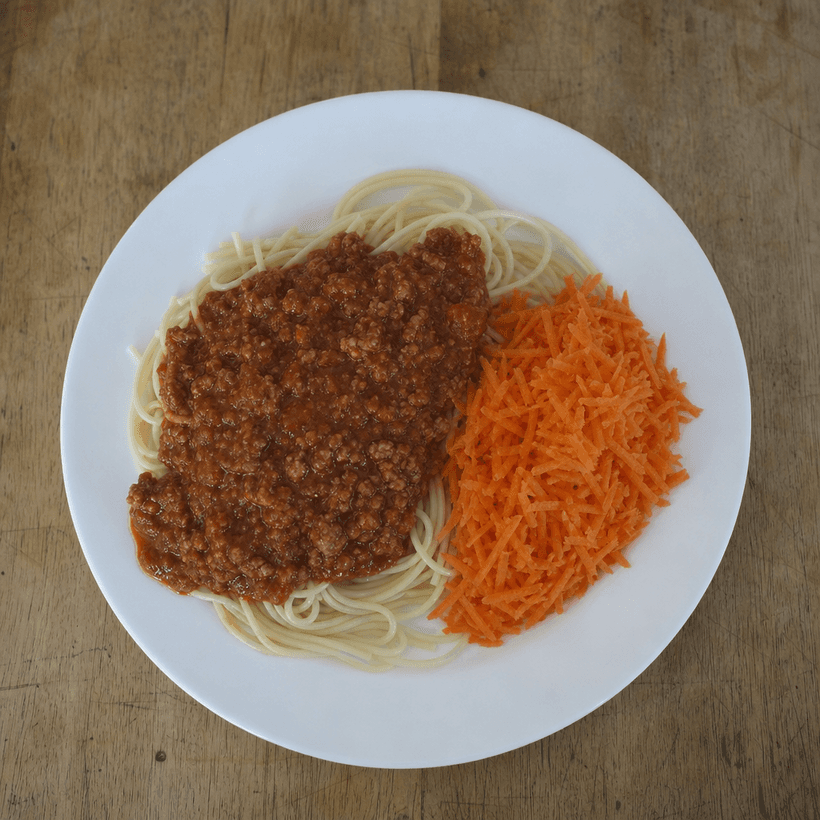 Spaghetti med kødsovs og revne gulerødder på en hvid tallerken