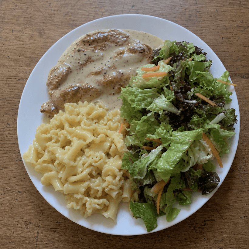 Kylling i flødesovs med pasta og salat på en hvid tallerken